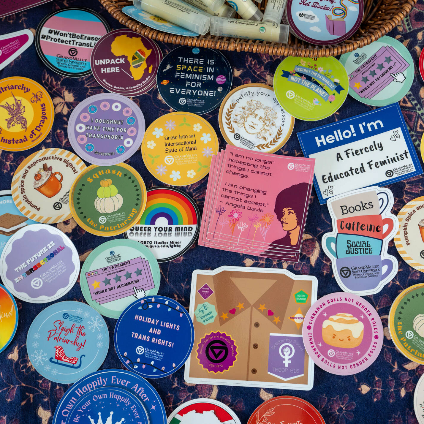 an assortment of stickeres featuring gender studies related sayings and images are arranged on a table, shown from above.